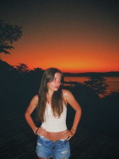 a woman standing in front of a sunset with her hands on her hips