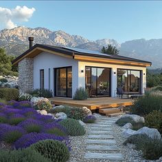 a house that is sitting in the middle of some bushes and flowers with mountains in the background