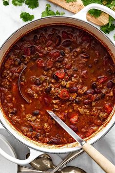 a large pot filled with chili and beans on top of a white table next to spoons