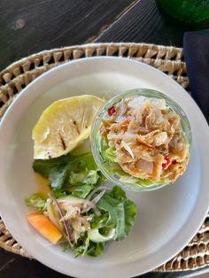 a white plate topped with salad next to a slice of lemon on top of a wooden table