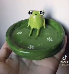 a small green frog sitting on top of a green plate in someone's hand