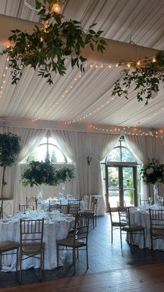 the inside of a wedding reception with white linens and greenery hanging from the ceiling