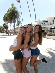 three girls are hugging on the beach with palm trees in the backgrouds