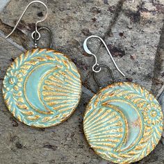 pair of earrings with gold and blue designs on them sitting on the ground in front of a stone wall