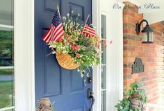 a blue front door with an american flag hanging from it's side and potted plants on the porch