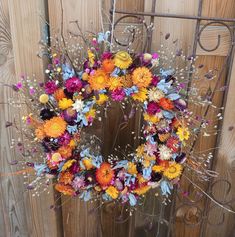 a colorful wreath is hanging on the side of a wooden fence with white and orange flowers