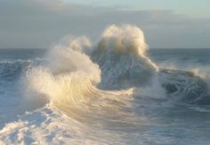 a large wave crashing into the ocean on a sunny day