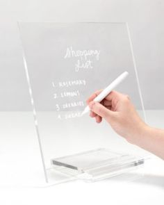 a person writing on a clear acrylic sign with a white pen in their hand