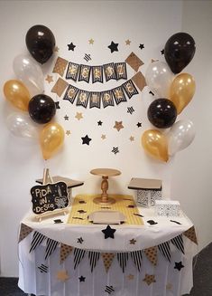 a table topped with black and gold balloons next to a wall filled with stars on it