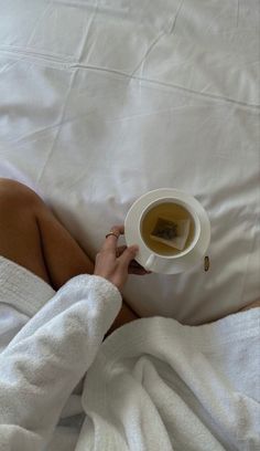 a person laying in bed with a cup of tea and saucer on their hand