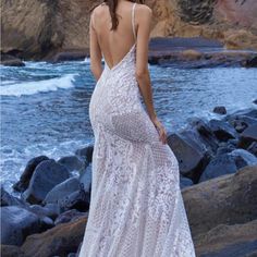 a woman in a white dress standing on rocks near the ocean with her back to the camera