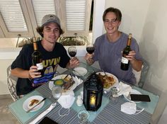 two men sitting at a table with wine and food