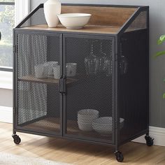 a metal cabinet with a wooden top and glass doors on wheels in front of a window