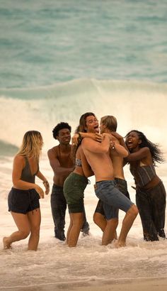 a group of people standing on top of a sandy beach next to the ocean with their arms around each other