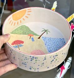 a hand holding a bowl with an image of a beach scene painted on it