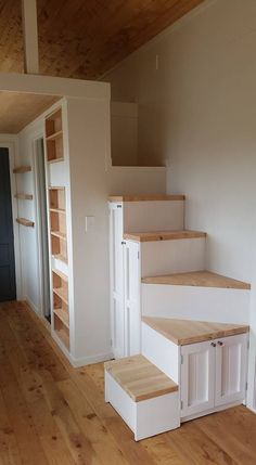 an empty room with wooden floors and white cabinets on either side of the stairs,