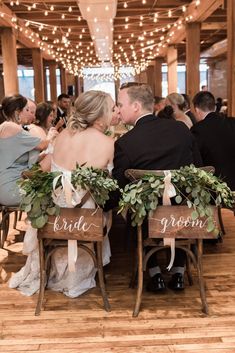 the bride and groom are sitting on their chairs at the wedding reception with greenery