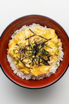 a red bowl filled with rice covered in sauce and topped with green onions on top