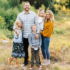 a family poses for a photo in an open field with trees and bushes behind them