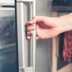 a person's hand is holding the handle on an appliance in a kitchen