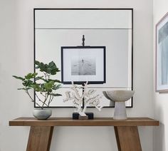 a wooden table topped with vases and plants next to a framed photograph on the wall