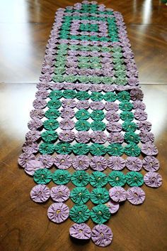 a table runner made out of purple and green paper flowers on a wooden floor in a room