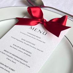 Black and white wedding menu card with a red satin bow. Shown on a white plate with a black rim alongside silver cutlery on a white cloth Christmas Table Setting Name Cards, Christmas Dinner Name Cards, Red Dinner Party Decor, Dinner Table Name Cards, Christmas Menu Card Design, Christmas Dinner Place Setting, Red And White Christmas Table Decor, Xmas Dinner Table Decoration, Christmas Decorations Restaurant