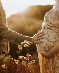 a pregnant woman holding her husband's belly in a field at sunset with the sun shining on them