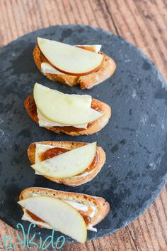 four pieces of bread with cheese and apple slices on them sitting on a black plate