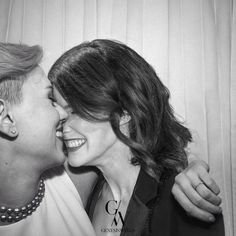 black and white photograph of two people kissing each other in front of curtained background