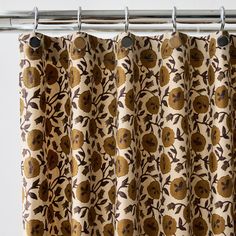 a curtain with an orange and brown flower pattern hanging from it's metal rod