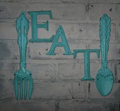 the letters eat and fork are painted turquoise on a brick wall with two green utensils