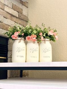 three mason jars with flowers in them sitting on a shelf next to a brick fireplace