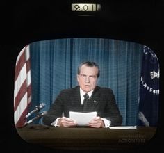 a man sitting at a desk with papers in front of him and an american flag behind him