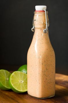 a glass bottle filled with dressing next to limes