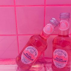 two bottles of liquid sitting on top of a pink tiled countertop next to each other