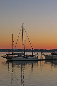 two boats are docked in the water as the sun is setting over the horizon behind them