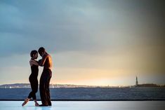 two people standing next to each other near the ocean