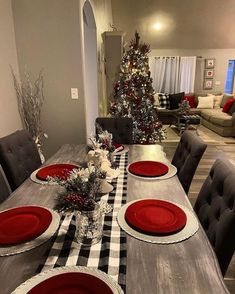 a dining room table set for christmas with red plates and placemats on it