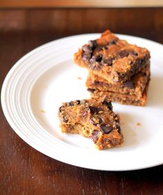 three pieces of chocolate chip cookie bars on a white plate with a wooden table in the background