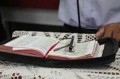 an open book is sitting on a table with a pen in it and someone's hand