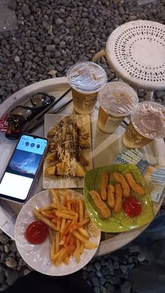 a table topped with plates of food next to glasses and a cell phone on top of it