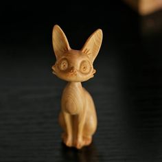 a small wooden toy cat sitting on top of a black table with its eyes open