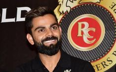 a man with a beard standing in front of a red and gold logo on a black background