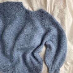 a blue sweater laying on top of a white sheet covered bed next to a pillow