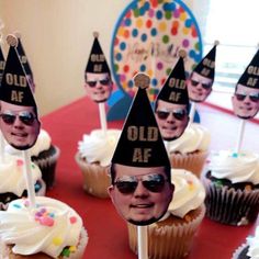 cupcakes with hats and sunglasses on them are sitting on a red tablecloth