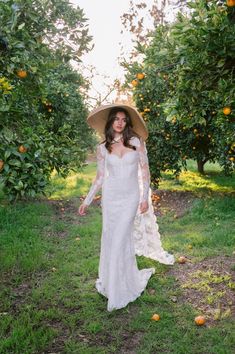 a woman in a white dress is holding an umbrella and walking through the orange trees