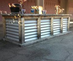 an outdoor bar made out of metal and wood with potted plants on the top