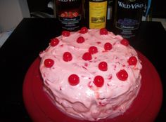 a cake with white frosting and red cherries on top, surrounded by liquor bottles