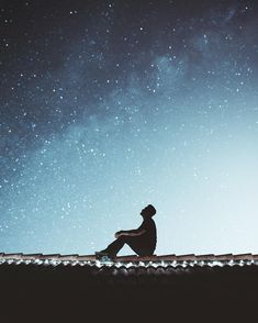 a man sitting on top of a roof looking up at the stars